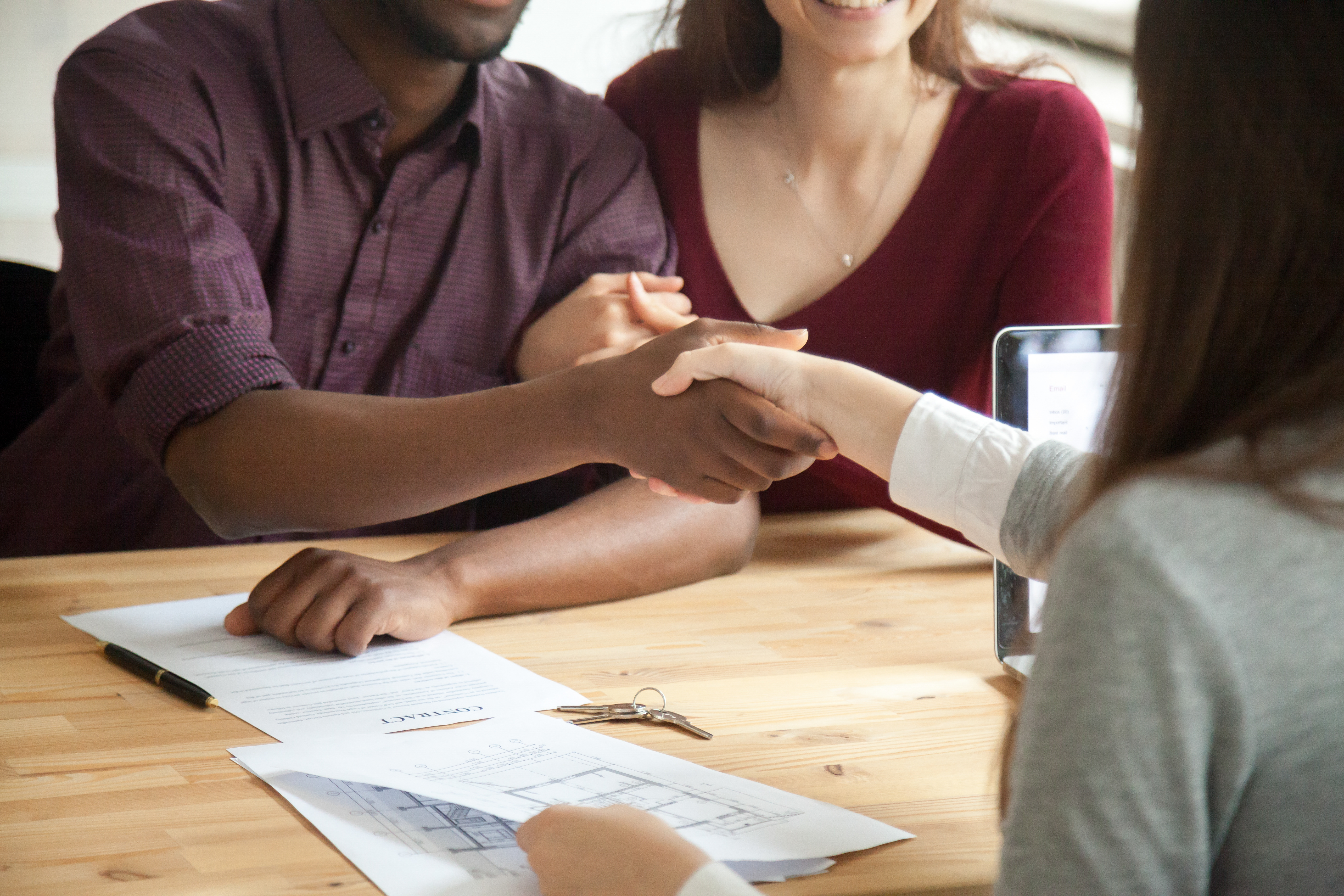 African american man shaking hands with real estate agent, contract and keys on table. Husband and wife signed rental agreement. Young multiethnic couple purchased new home concept. Close up view